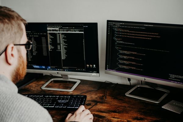 Software developer working on code with dual monitors in a home office setting.