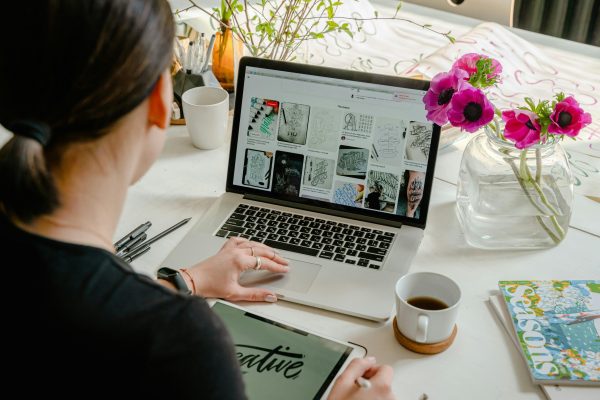 Woman in a creative workspace using a laptop and tablet for calligraphy. Artistic and tech-driven environment.